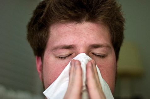 A cold man sneezes in a tissue.