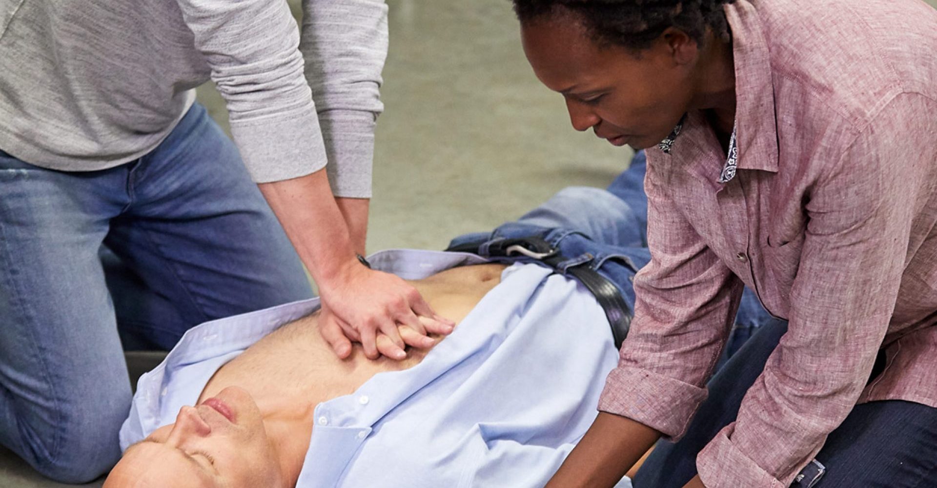Two people help save a life by using an AED and doing chest compressions on a colleague.
