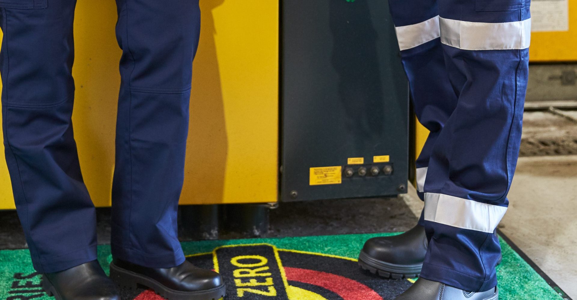 Staff members in sturdy shoes and wearing work uniforms, stand on a branded. dust mat or dirt control mat at work.